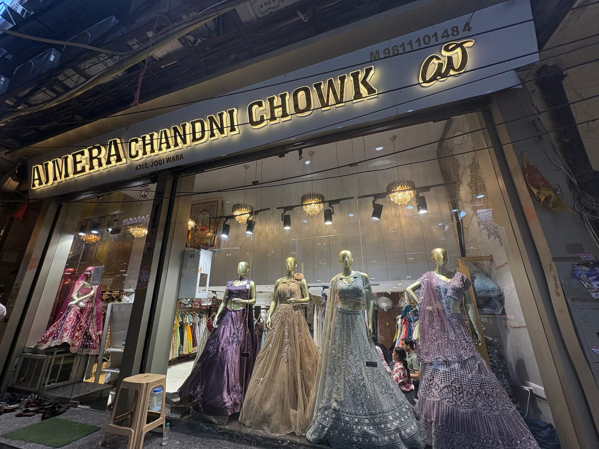 Ajmera Chandni Chowk shopfront at dusk: the lit sign above a window of four mannequins in lehengas, 4310 Jogiwara Gali