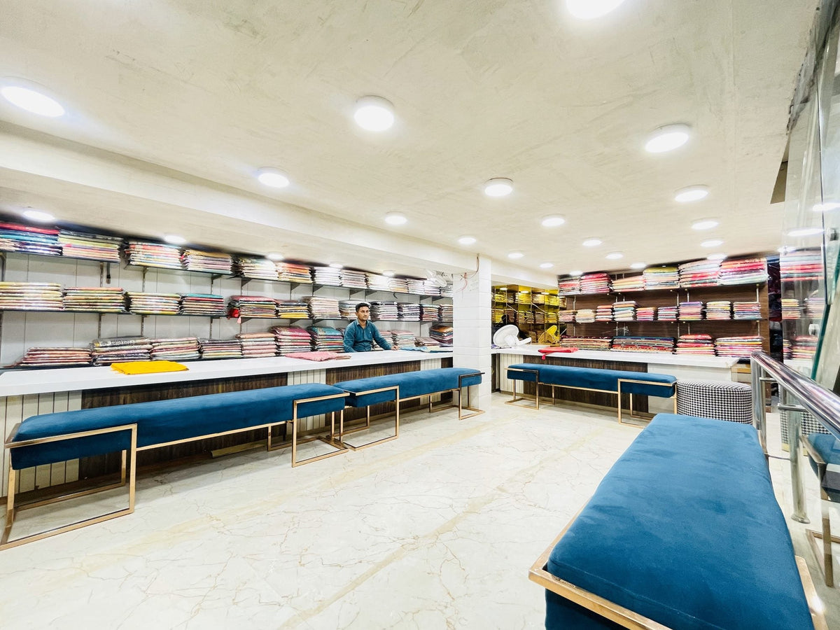 Ajmera's saree hall: long white counters, teal benches and shelves of folded sarees