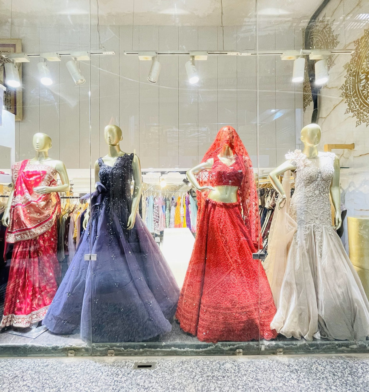 Ajmera's shop window by day: a pink saree, a navy gown, a red lehenga and an ivory fishtail gown